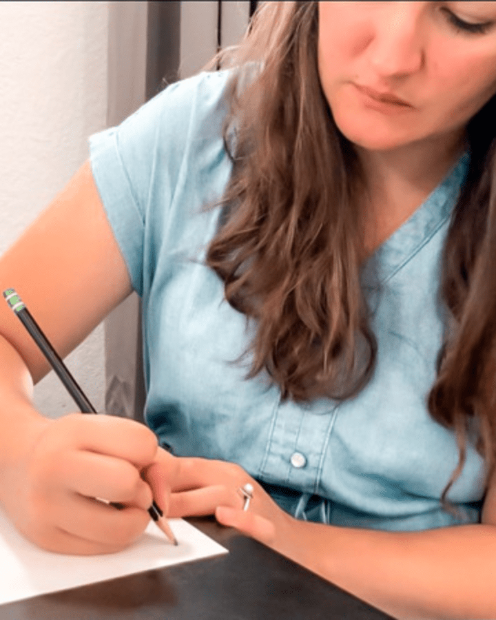 woman writing notes on paper with a pencil